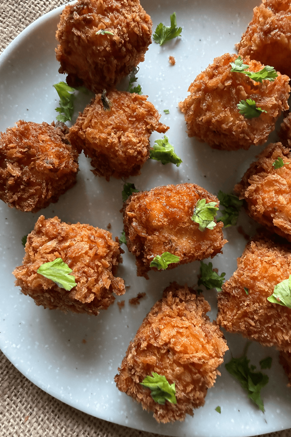 Close-up of crispy paneer popcorn with a crunchy coating, garnished with fresh coriander and served on a white plate over a rustic background.