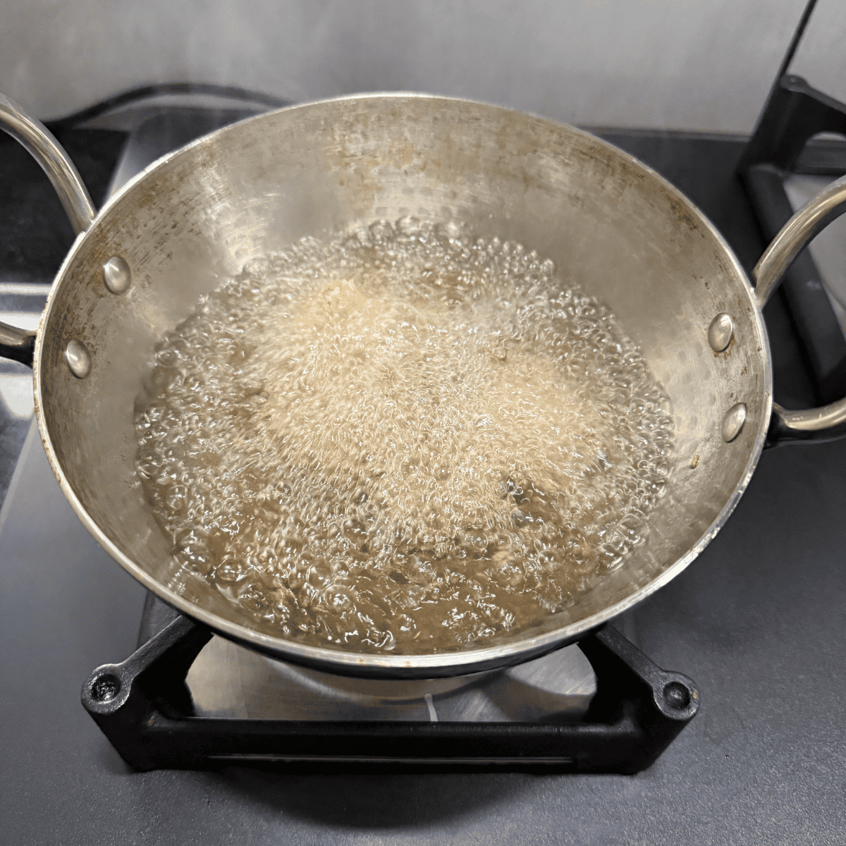 Paneer popcorn deep frying in hot oil in a steel kadai on a stovetop, with oil bubbling vigorously during cooking.