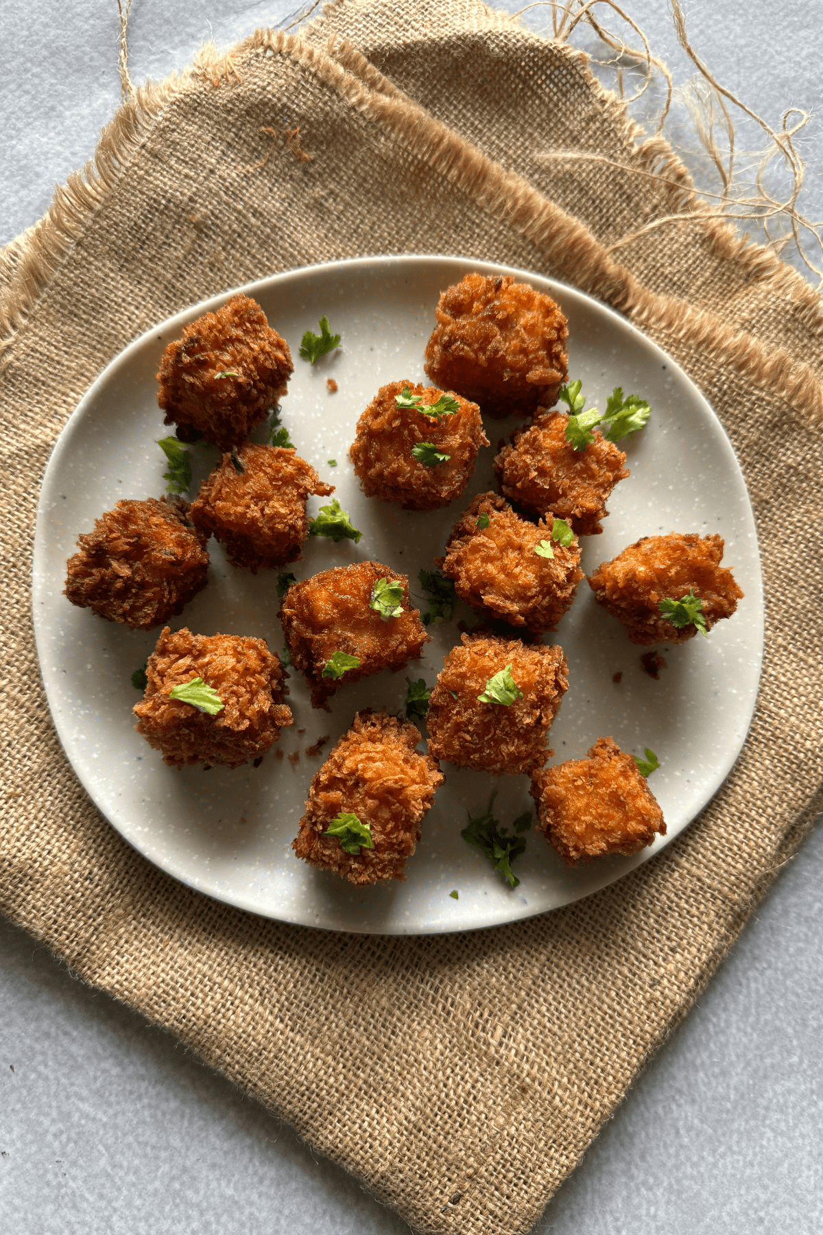 Crispy golden paneer popcorn bites garnished with coriander, served on a white plate over a rustic burlap cloth.
