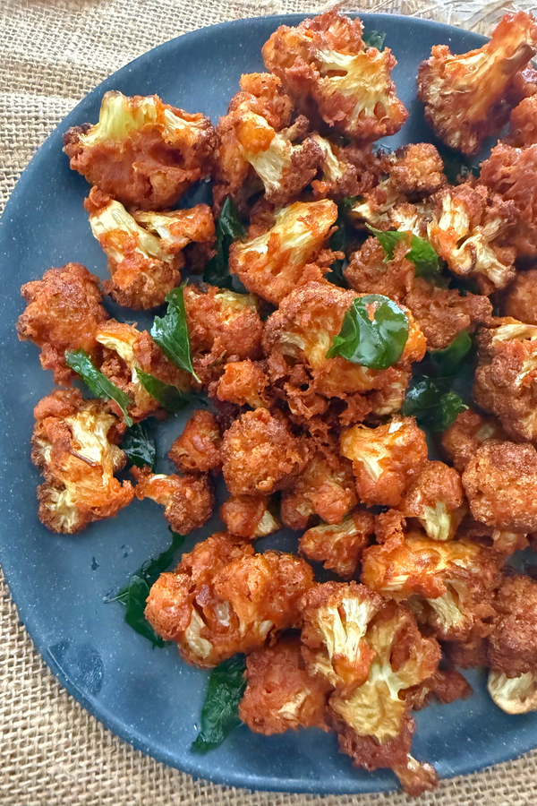 Golden brown cauliflower 65 on a plate with curry leaf ganished on top