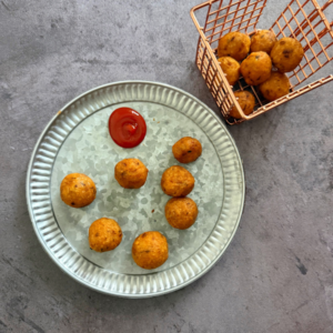 Crispy and golden brown potato balls served on a plate with kwtchup on the side