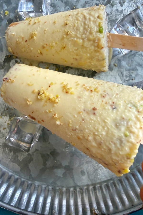 Close up of Kesar malai kulfi garnished with powdered nuts served on a plate with ice cubes